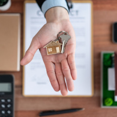 Pessoa segurando chave com pingente de casa sobre mesa com contrato, representando mudança de imóvel e intenções de aluguel no Brasil em 2025